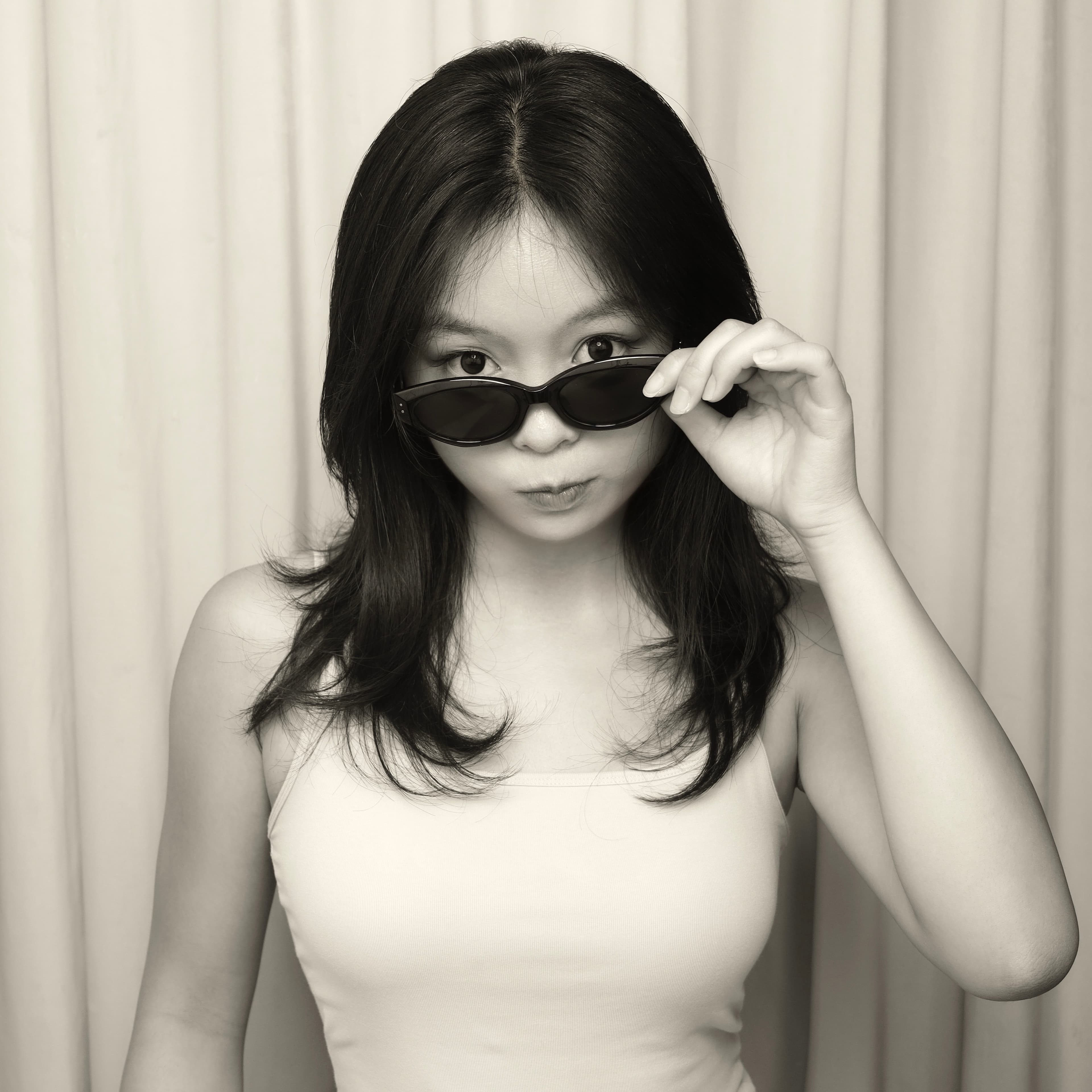 Alina looking over her sunglasses in front of curtains